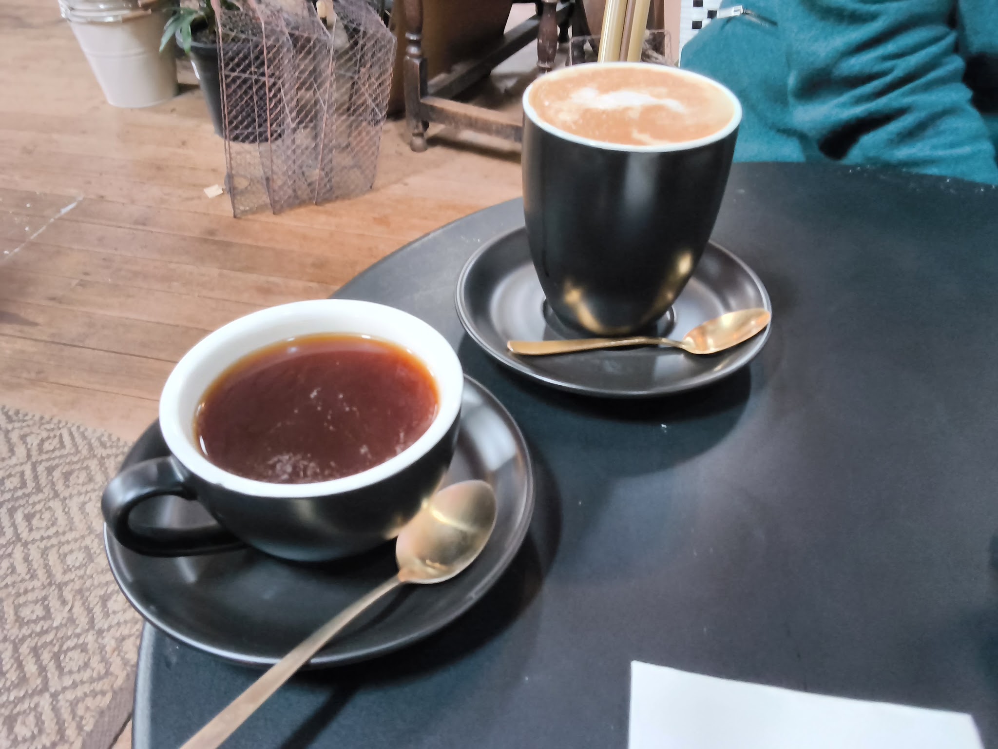 Two coffees in black cups with gold spoons